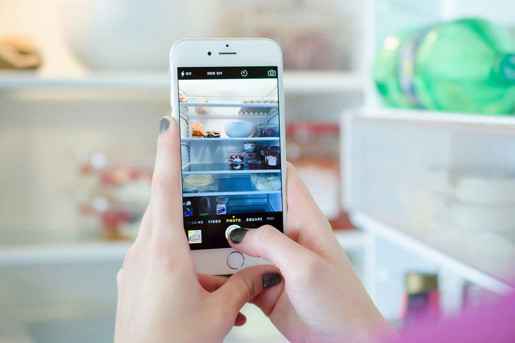 Person taking a photo of the inside of a fridge with a cell phone.