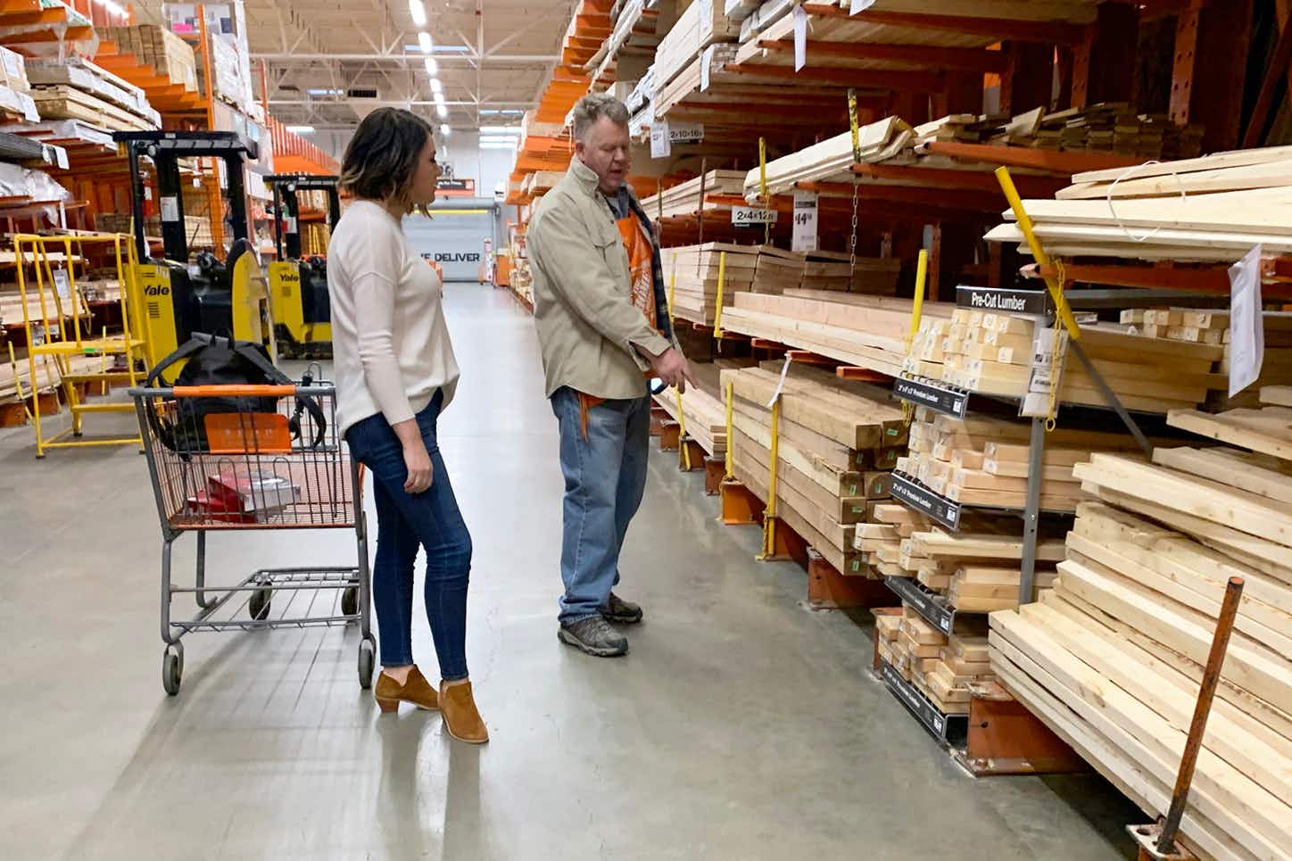 A woman talking with a Home Depot employee in the lumber section.