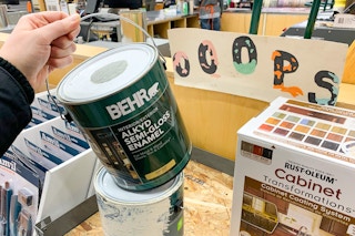 A person holding a gallon can of Behr paint