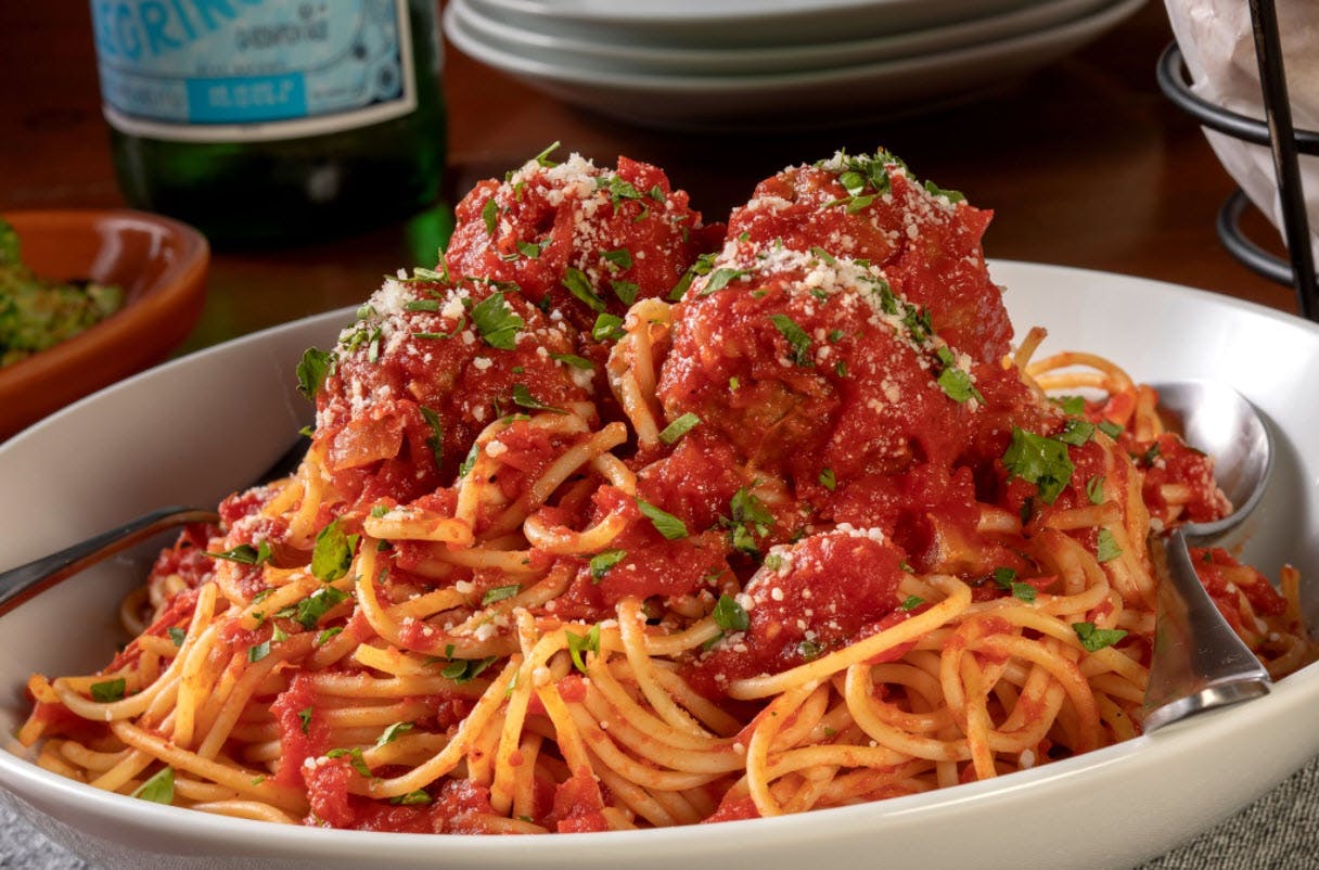A big plate of spaghetti and meatballs sitting on a table in a restaurant.