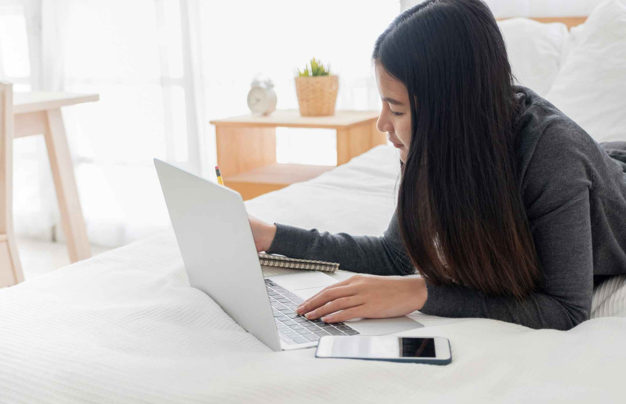 person on bed with laptop and notebook