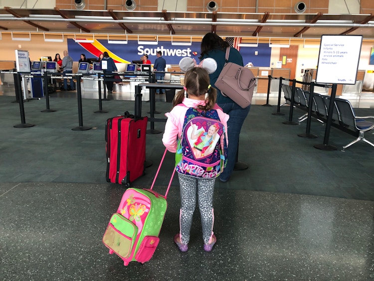A little girl stands in line with luggage to go to Disneyland.