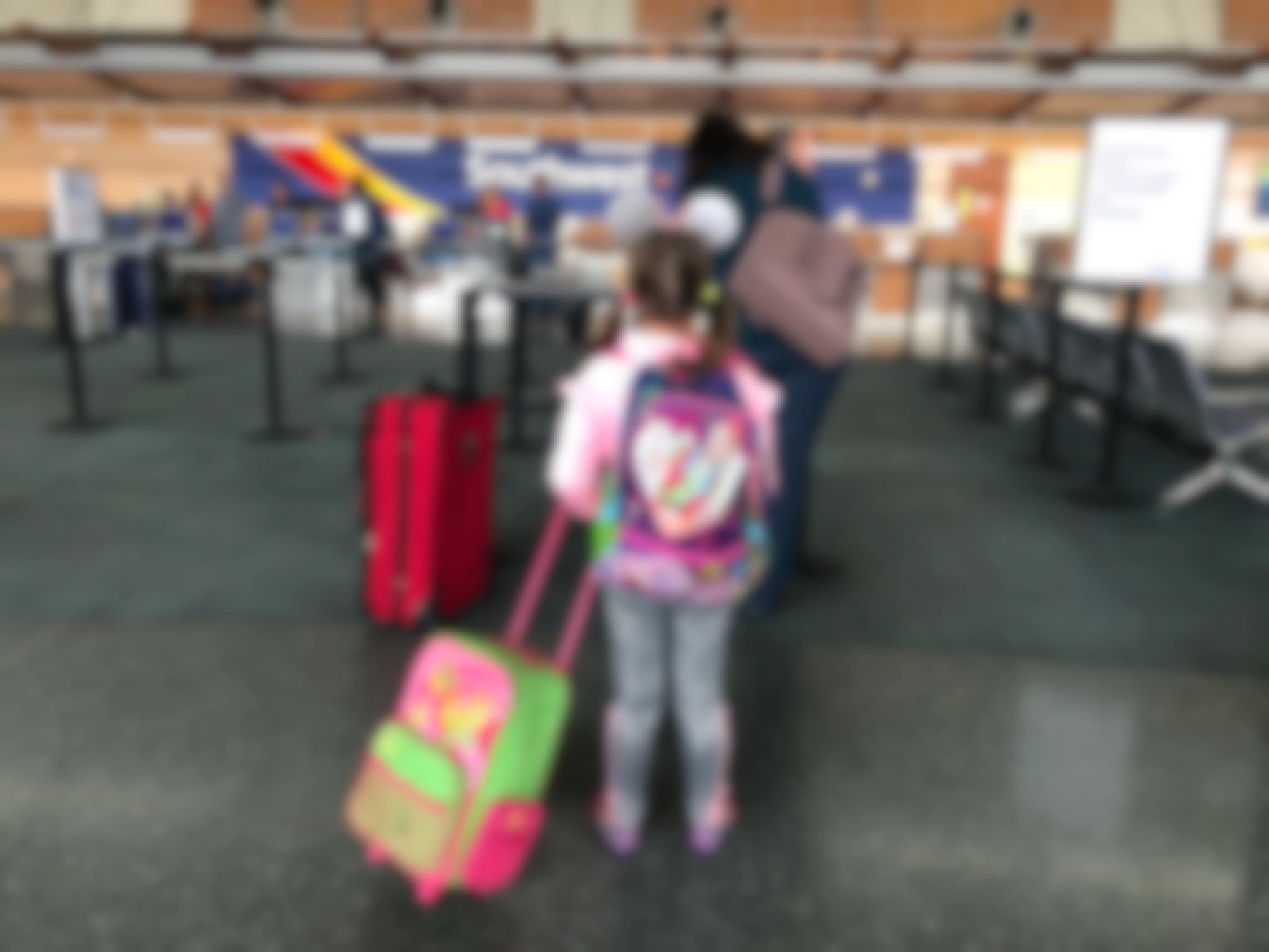 A little girl stands in line with luggage to go to Disneyland.