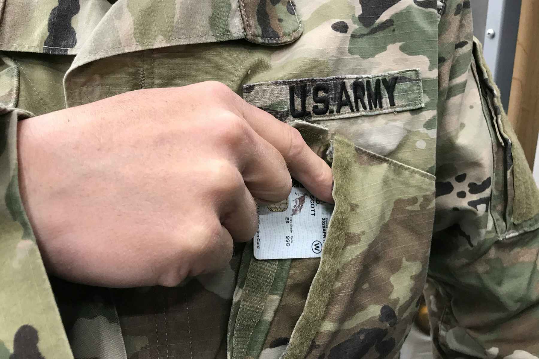 A person in US Army fatigues pulls a military ID from their front shirt pocket