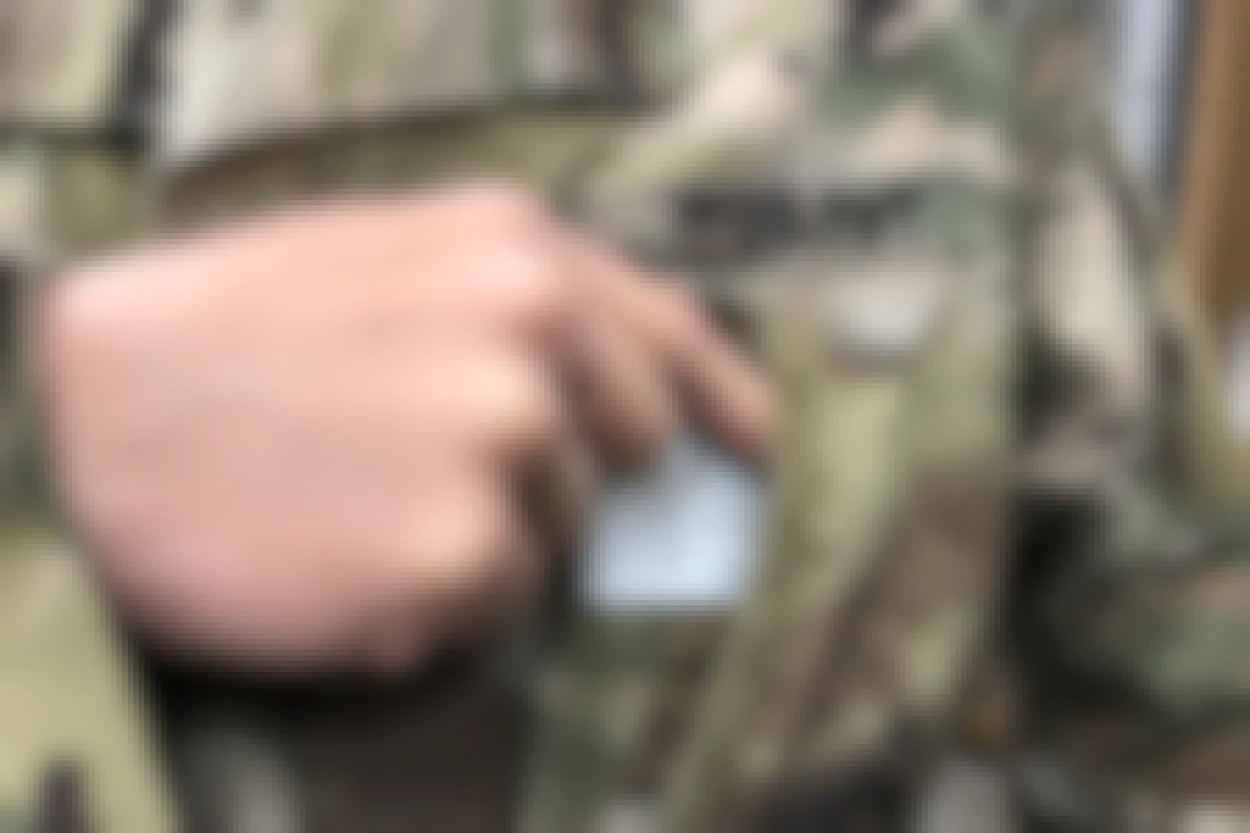 person in US Army fatigues pulls a military ID from his or her front shirt pocket