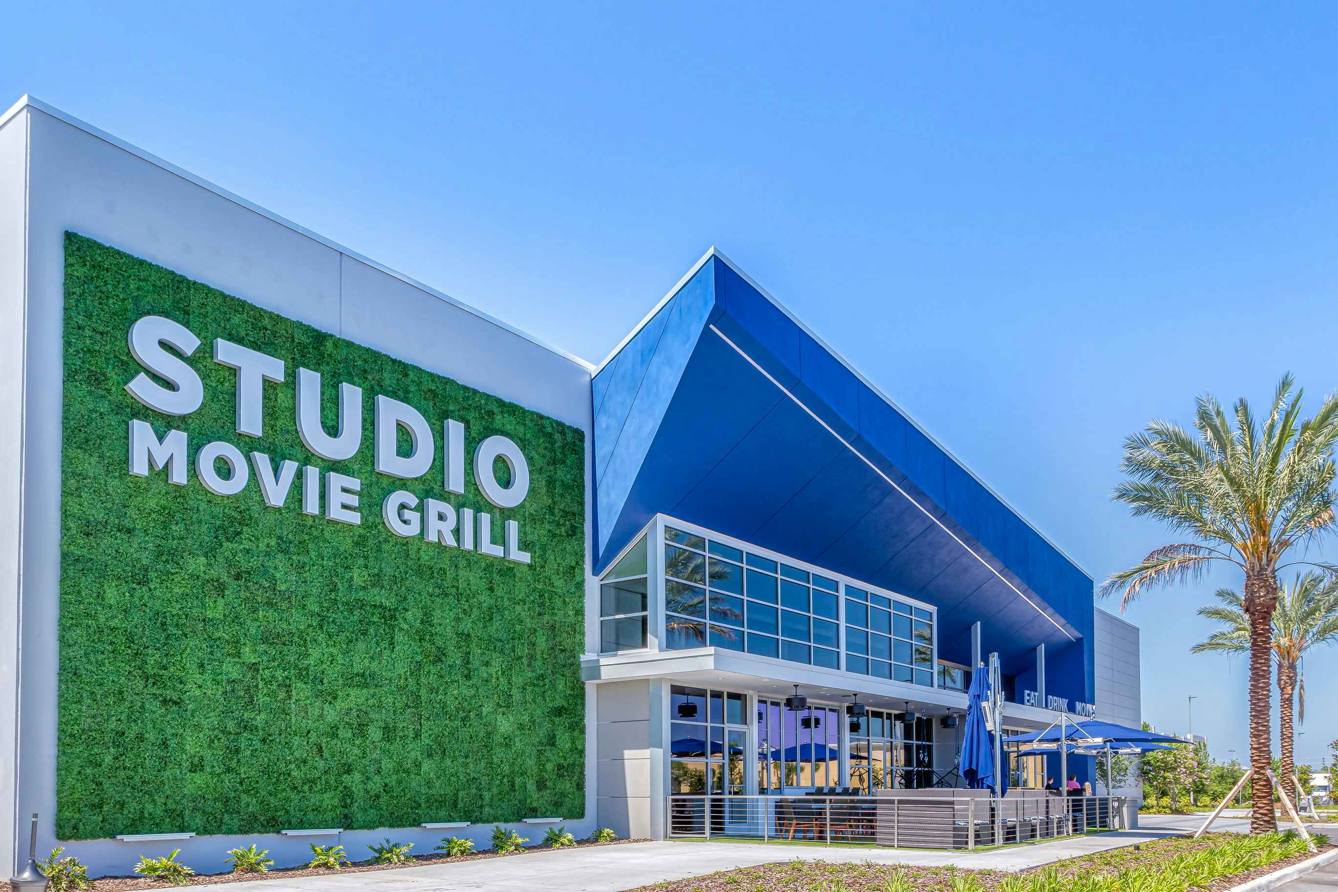 View of Studio Movie Grill entrance outside with parasols and palm trees