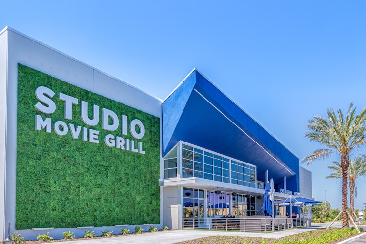 View of Studio Movie Grill entrance outside with parasols and palm trees