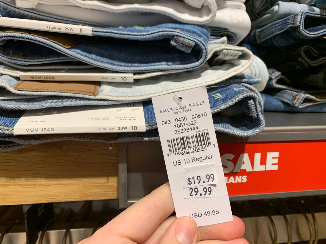 A person holding a price tag with a clearance sticker on a pair of jeans.