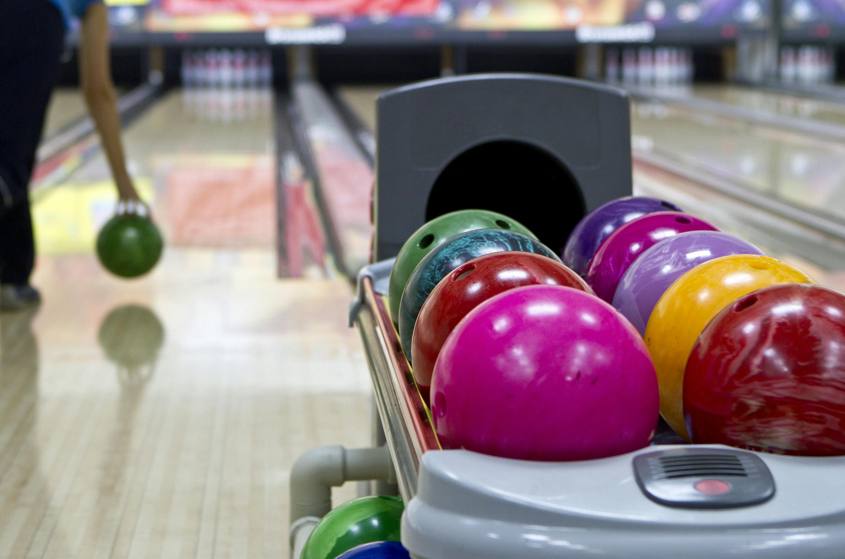 Bowling balls at a bowling alley with a person in the background about to throw their ball down the alley