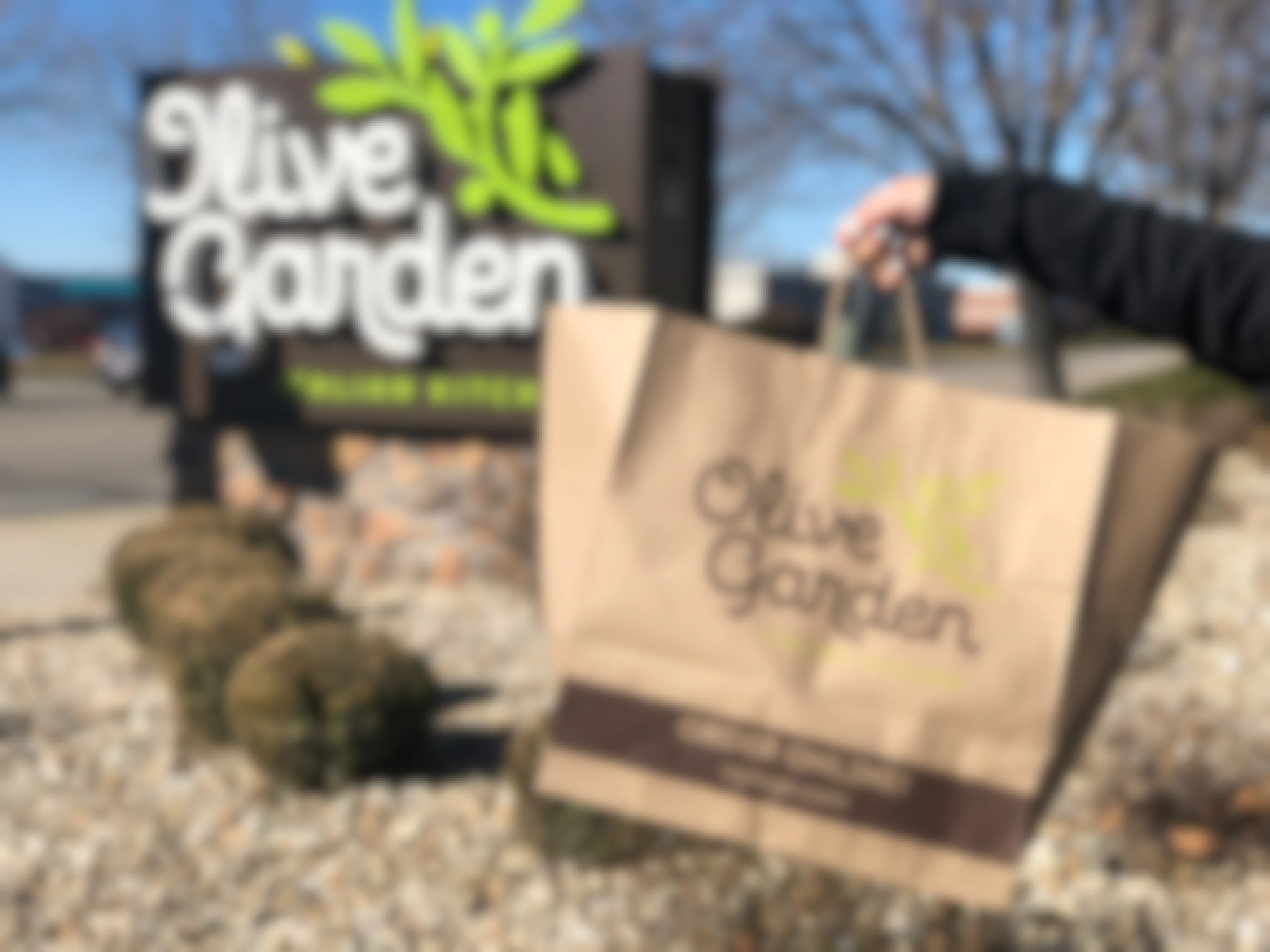 Someone holding an Olive Garden to go bag in front of an Olive Garden sign