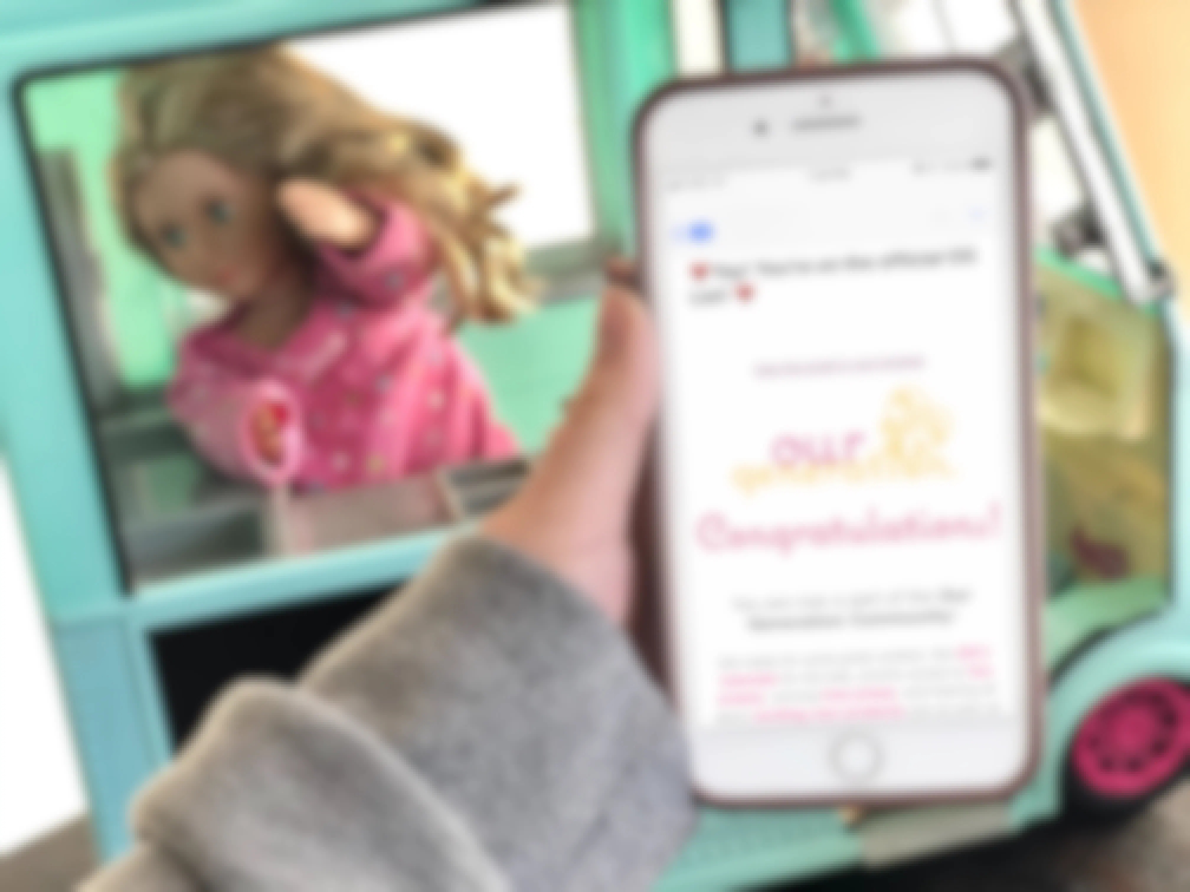 The Our Generation Doll email newsletter displayed on cell phone in front of a doll .