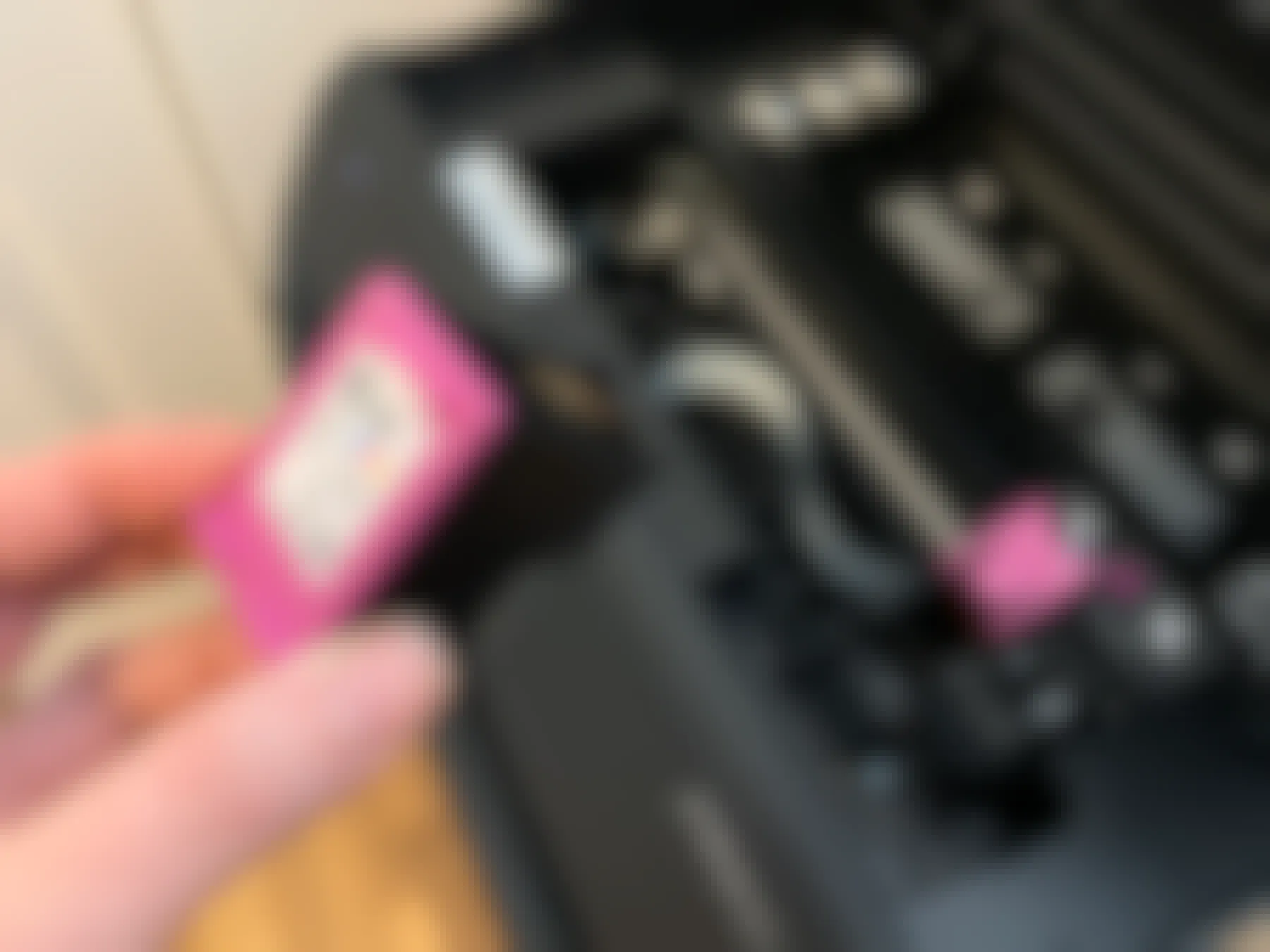 A hand holding an HP color printer ink cartridge in front of a printer.