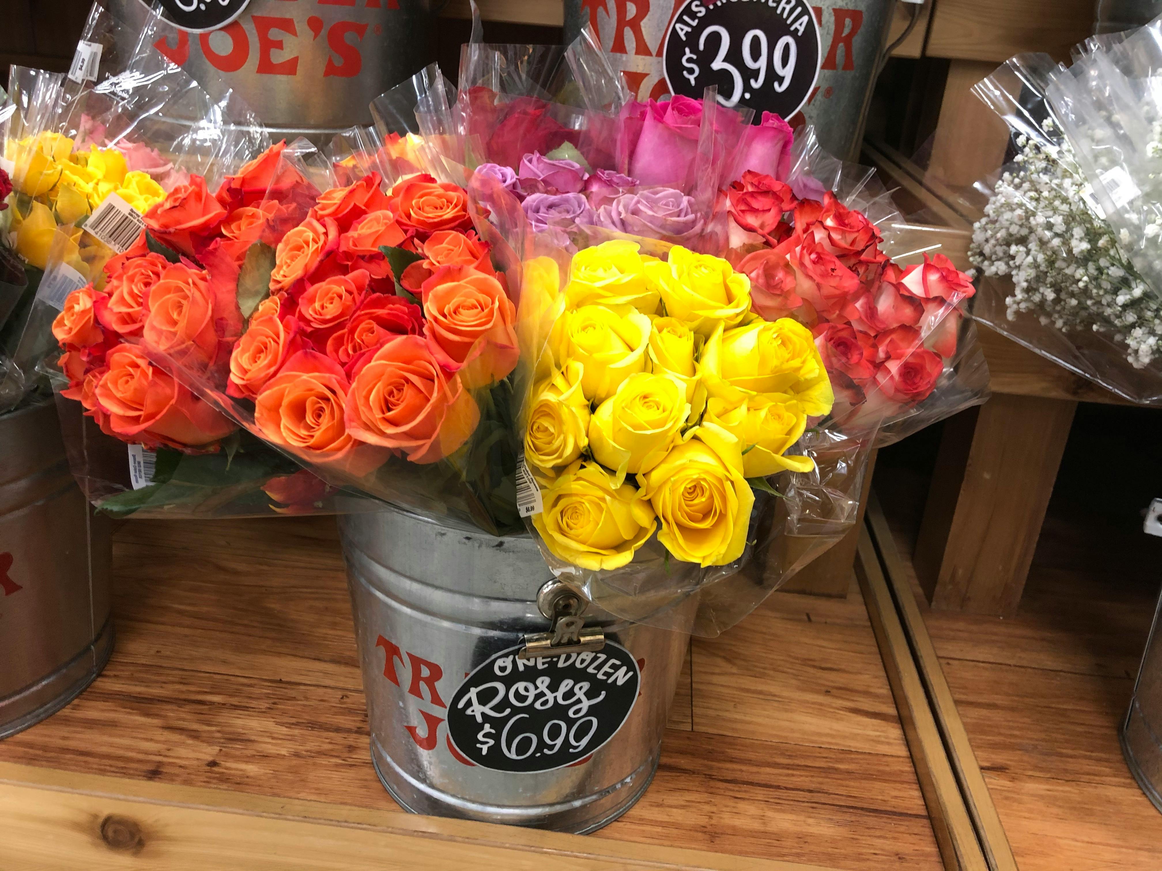 A bucket holding orange, yellow and red roses inside a Trader Joe's.