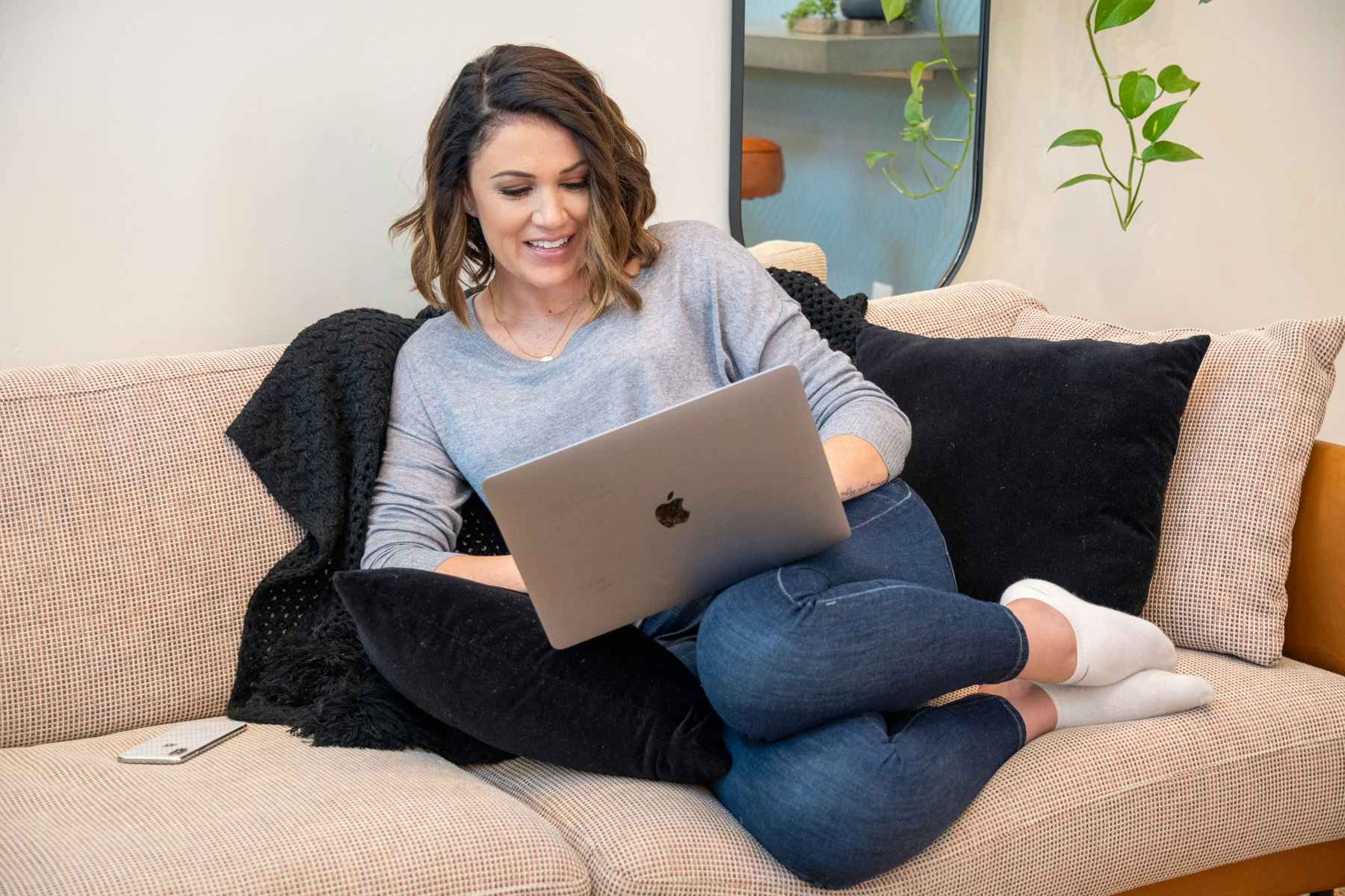 A woman sitting on a sofa using an apple laptop.