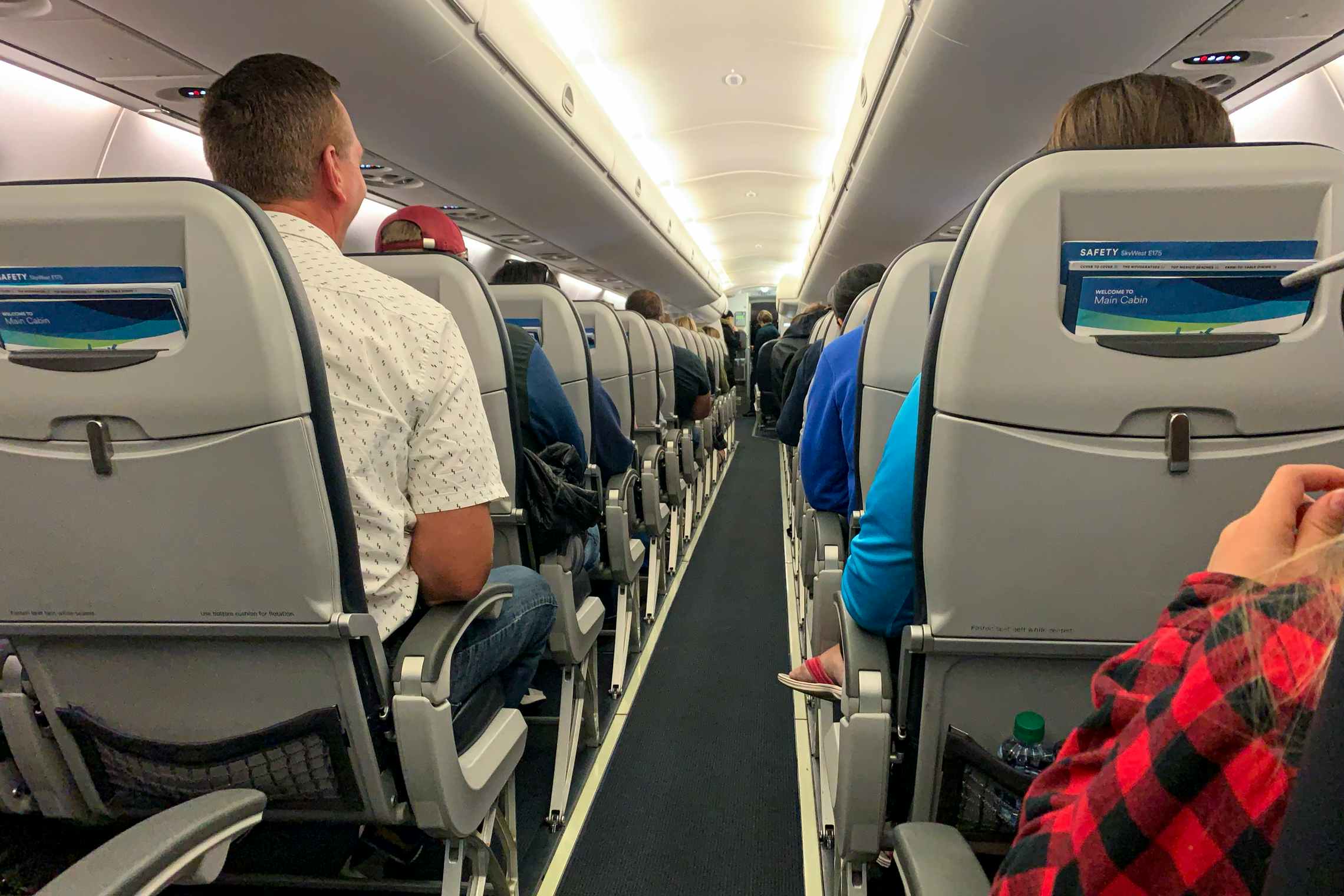An aisle of the plane showing the backs of seats filled with passangers.