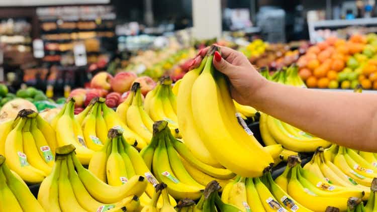 Hand picking up one bunch of bananas inside a grocery store.
