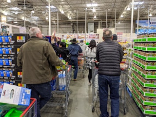 Customers with baskets full of food standing in a long line at Costco checkout.