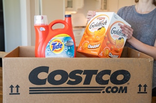 A woman pulling gold fish crackers and tide from a Costco.com shipping box.
