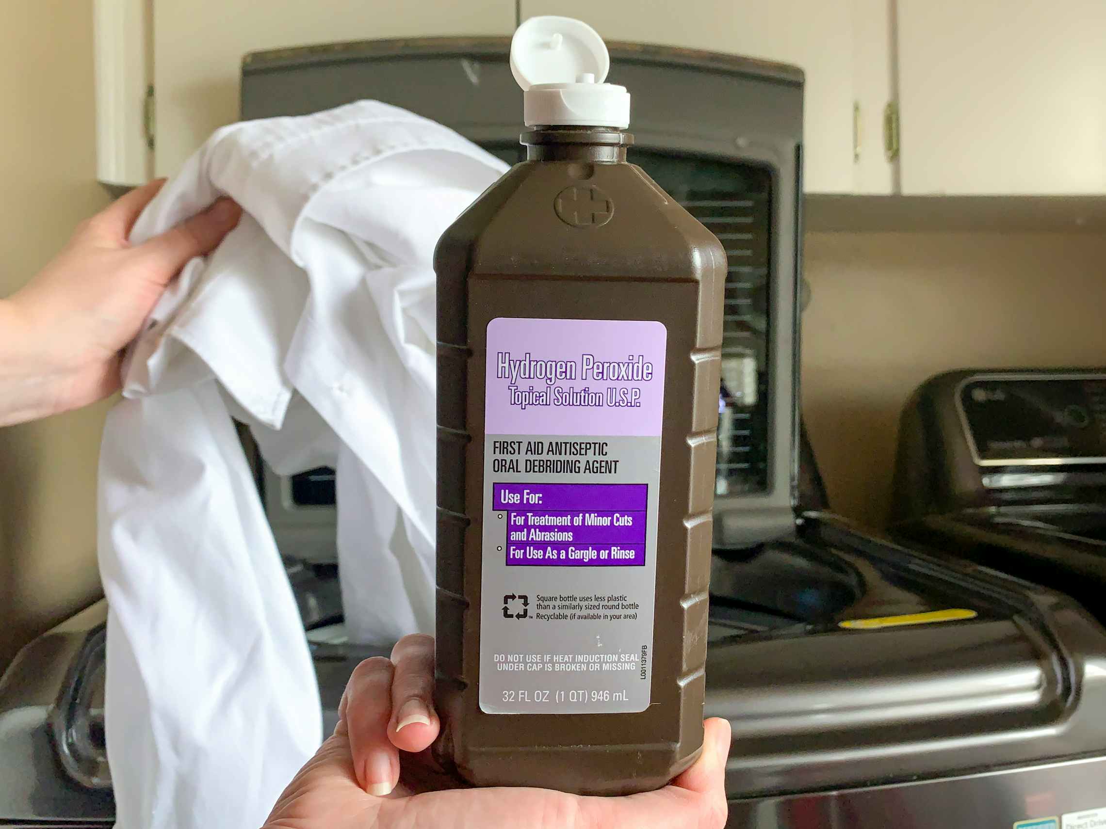 hydrogen peroxide held in front of a washing machine, with white clothes being tossed in.