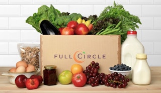 Full Circle box of fresh produce with eggs, milk, nuts, and jam on kitchen table.