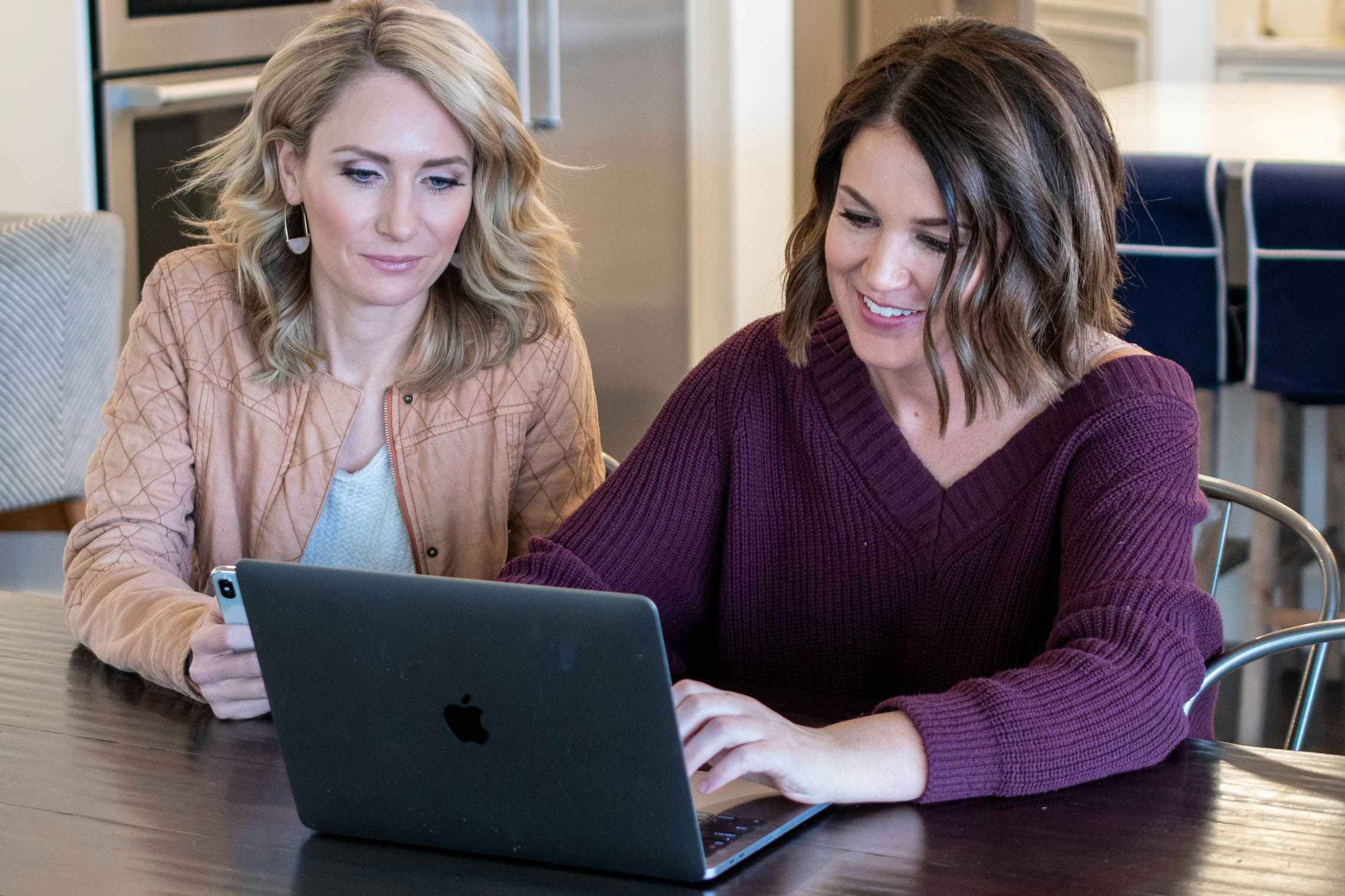 Two women sitting at a table looking at something on a laptop.