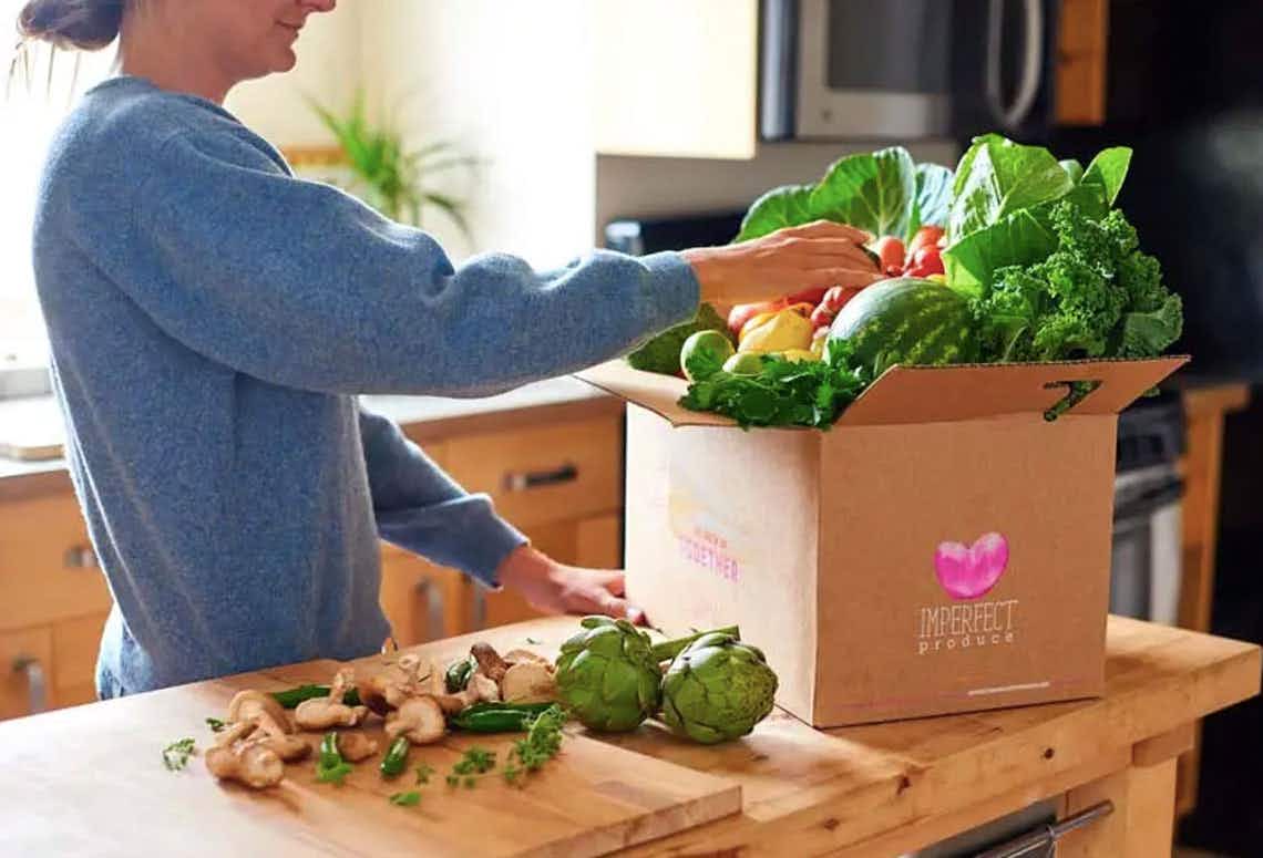 Woman pulling fresh produce from an Imperfect Foods box in kitchen.