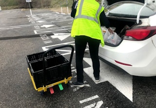 Grocery store associate loading groceries into the back of a white car.