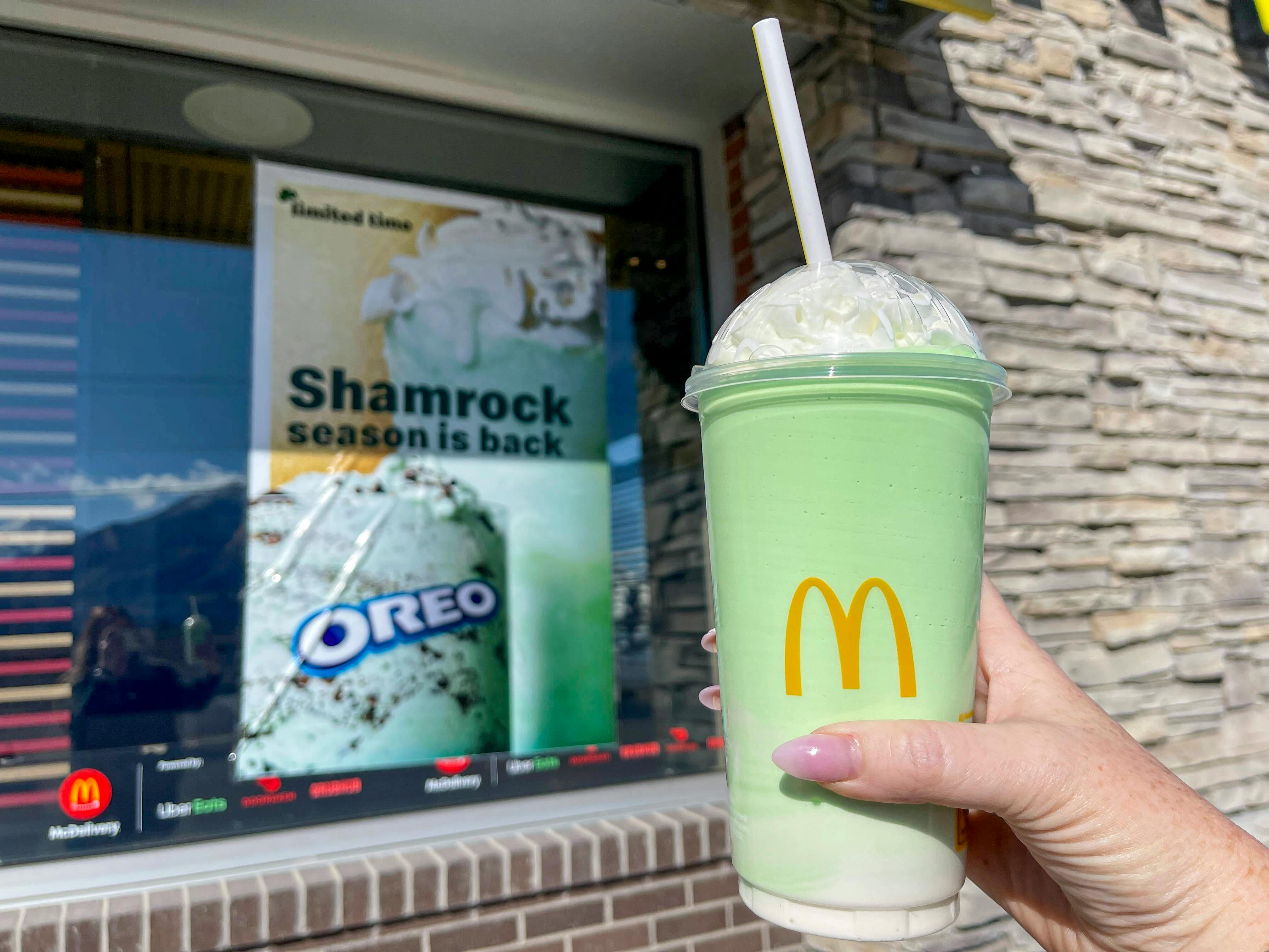 A person holding a shamrock shake in front of a McDonalds restaurant.