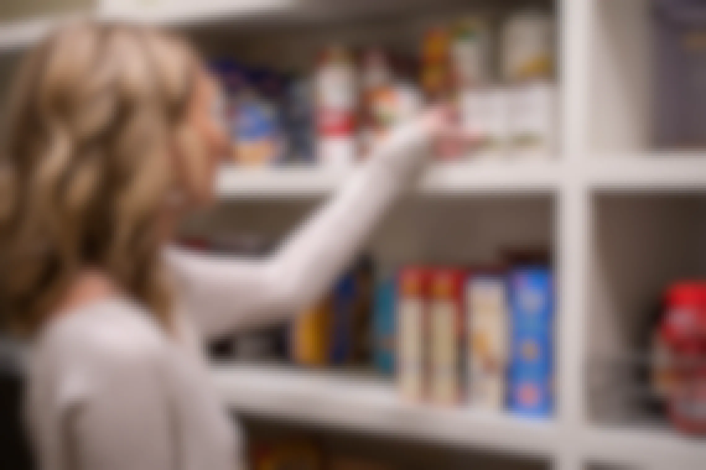 Woman loads non-perishable foods on to the shelves in a pantry.