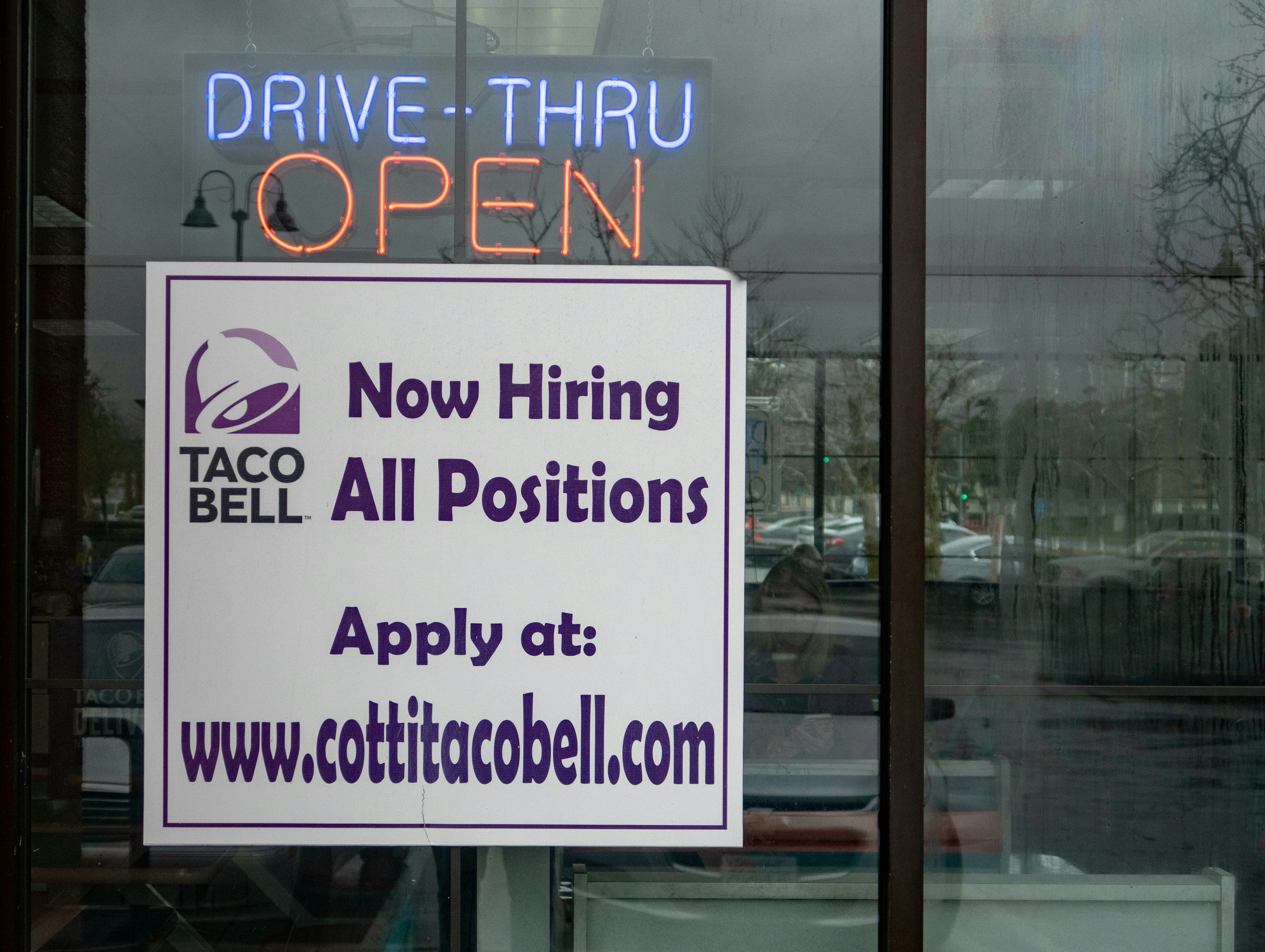 A sign in a Taco Bell window that reads, "Now Hiring All Positions