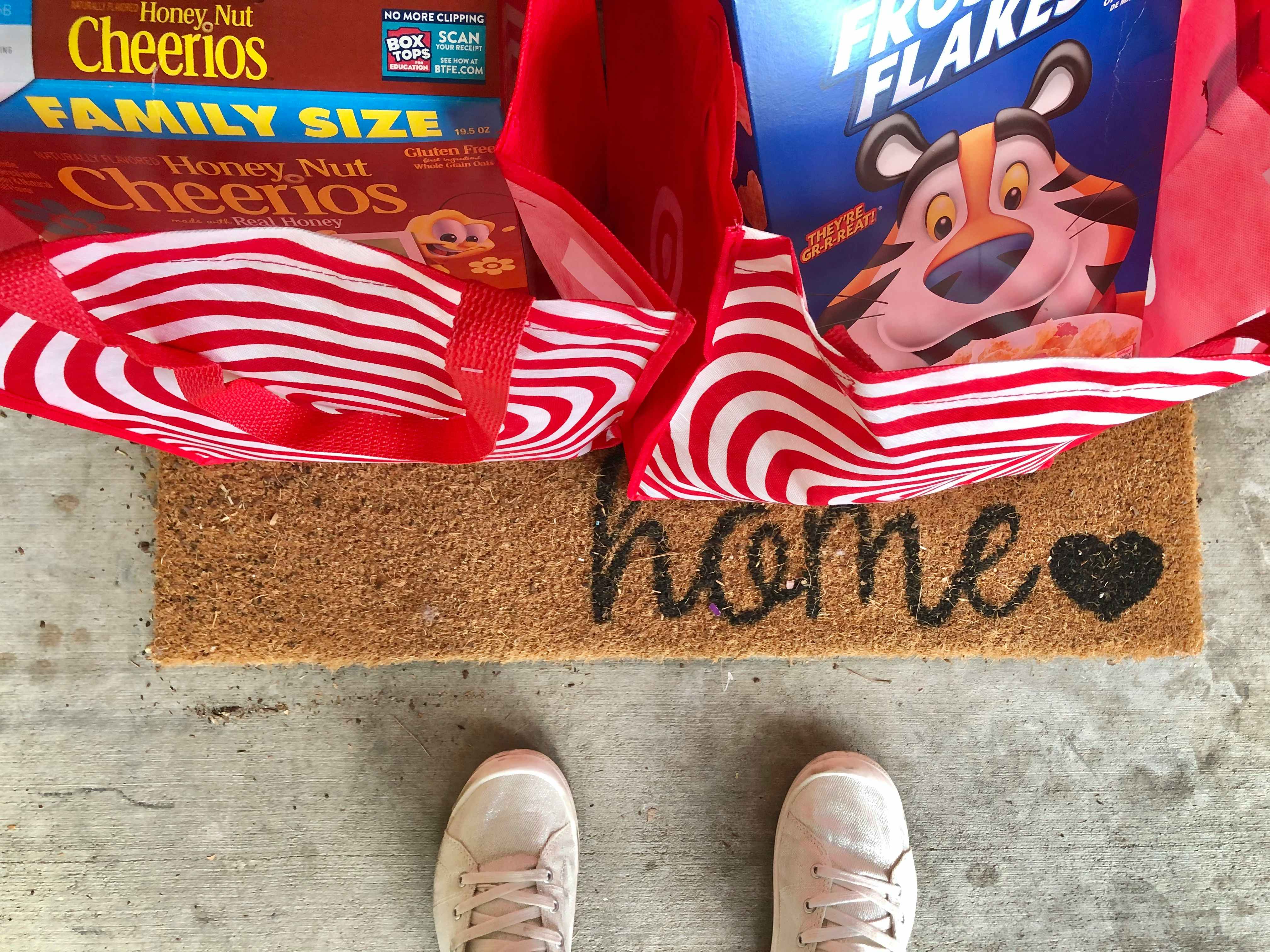 Woman standing over Target reusable bags with cereal on front doorstep.