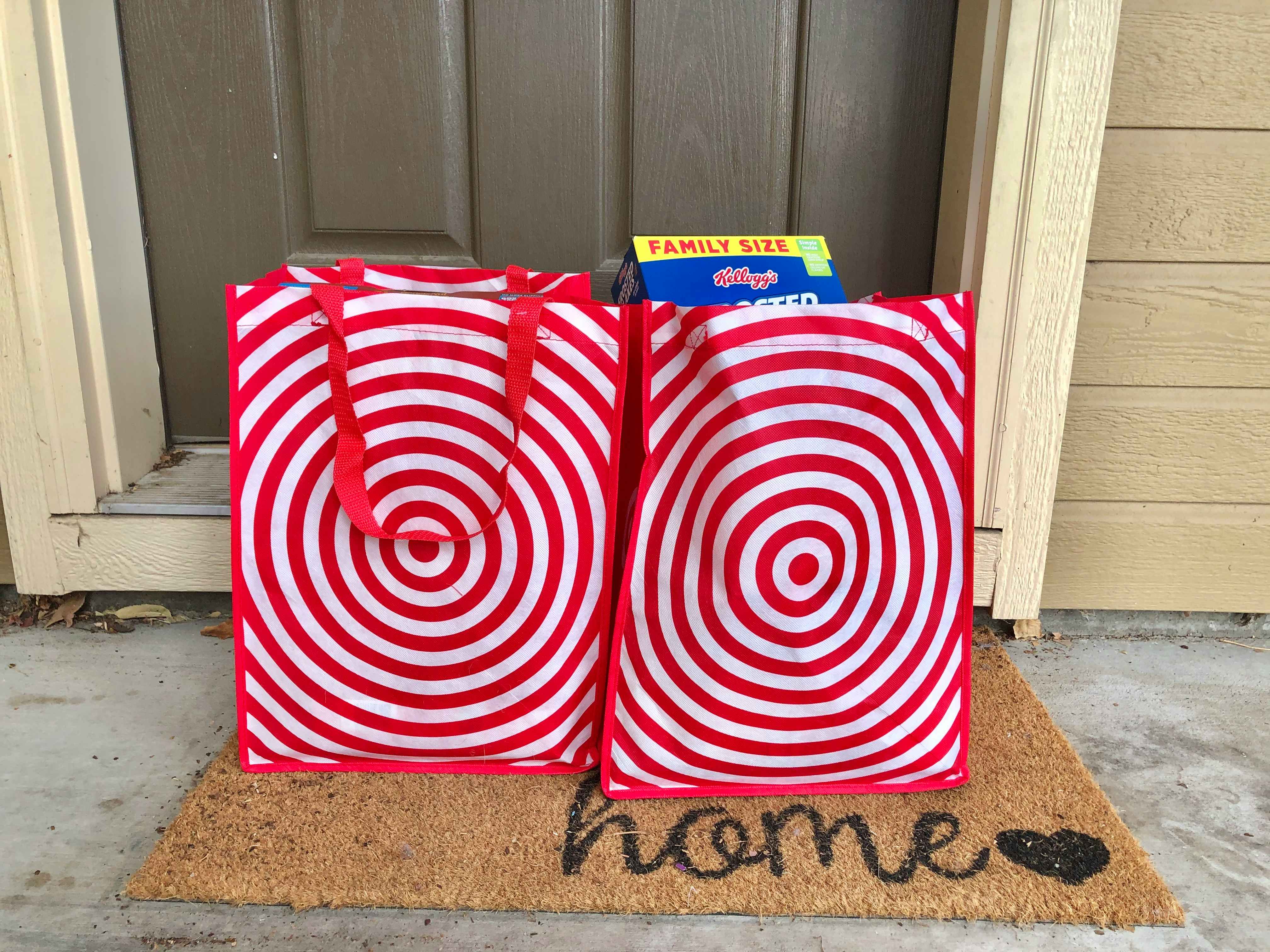 Two Target reusable grocery bags on a welcome mat on front doorstep.