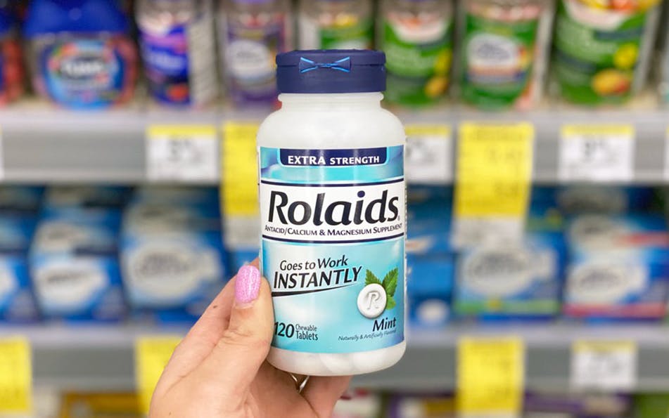A person's hand holding up a bottle of Rolaids in front of a shelf in Walgreens.