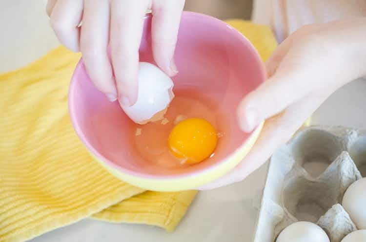 Person-removing-bits-of-eggsheel-from-cracked-eggs-in-a-bowl-using-another-piece-of-eggshell