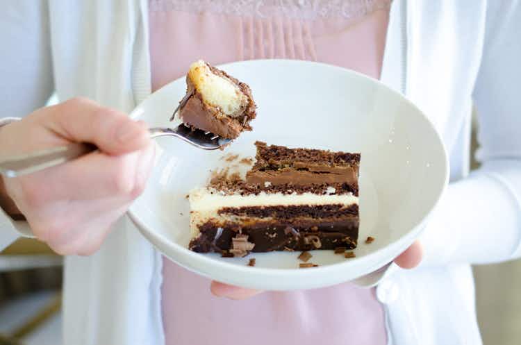 A-woman-holding-a-plate-with-a-slice-of-cake-with-a-bite-of-it-on-her-fork