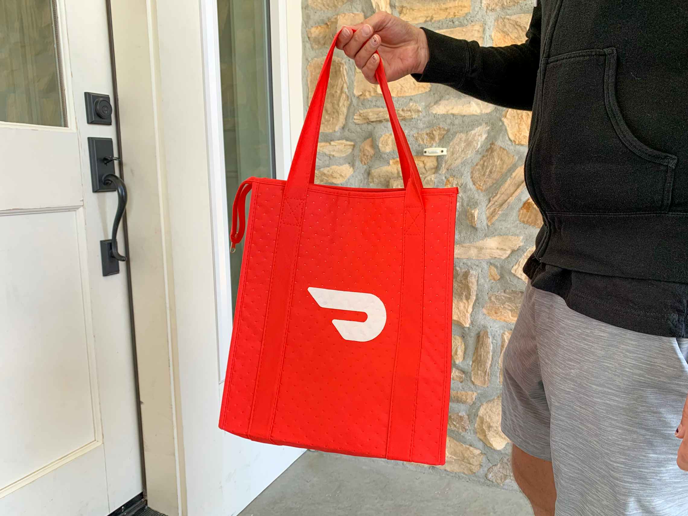 A person holding up a Doordash delivery bag outside of a front door.