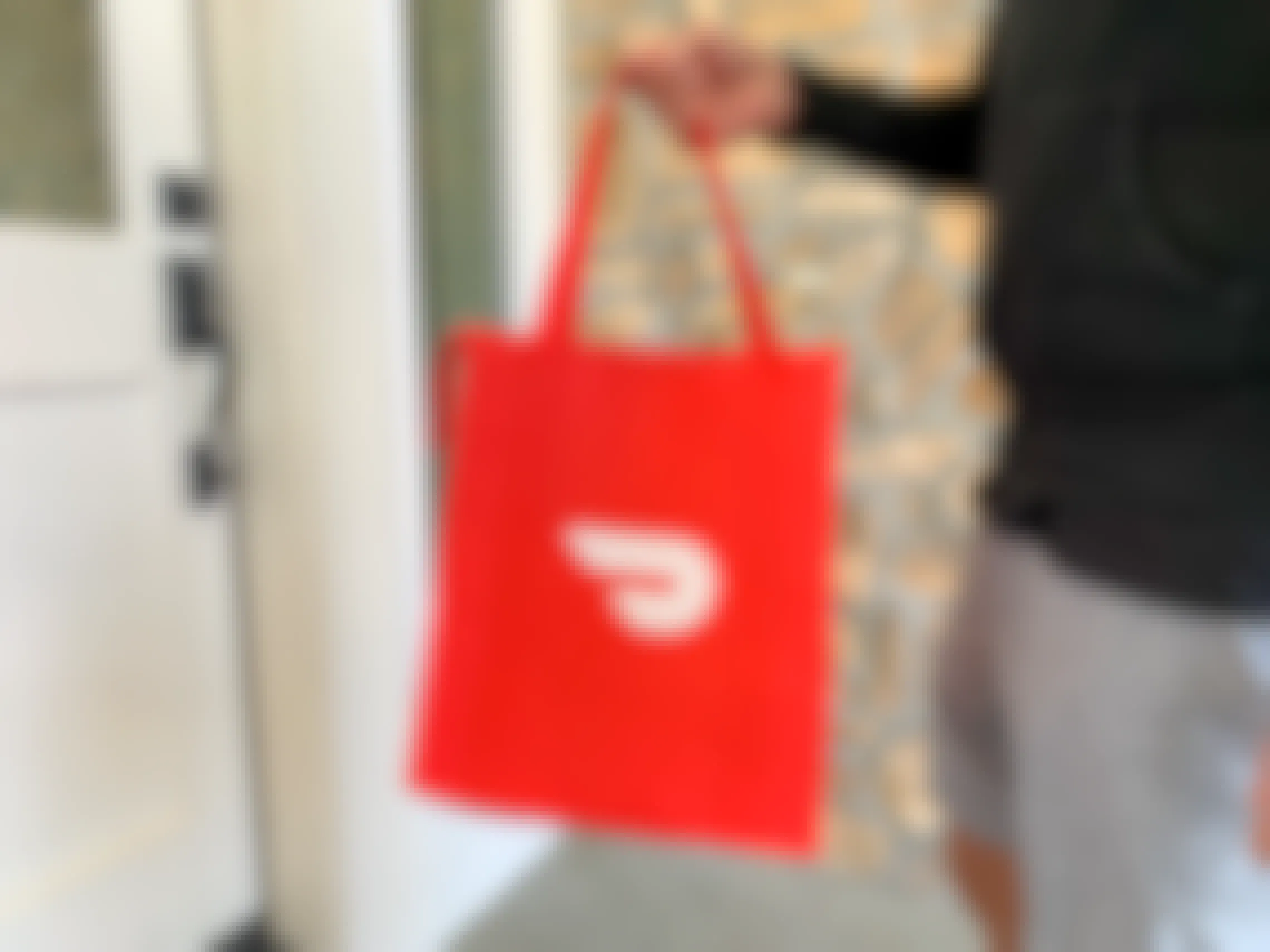 A man standing on a front porch delivering food in a doordash bag