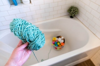 An Easter basket hidden in a bathtub with a string of yarn attached to it and the ball of yarn held in someones hand.