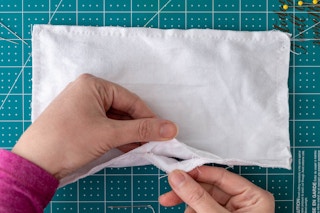 hands showing the opening the the fabric used to turn the mask, right side out.