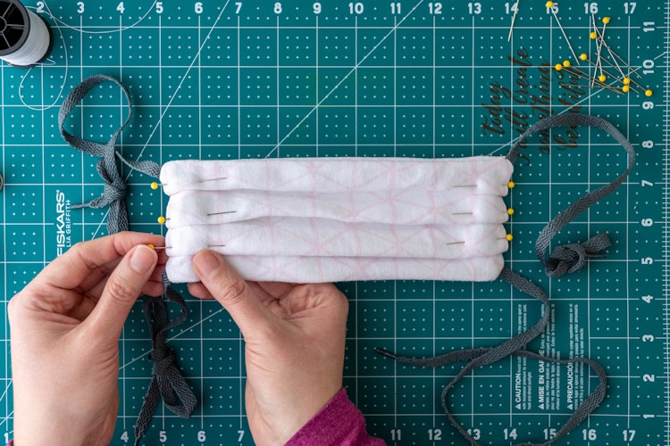 Pinning three pleats or folds lengthwise in the mask so it fits on a face securely.