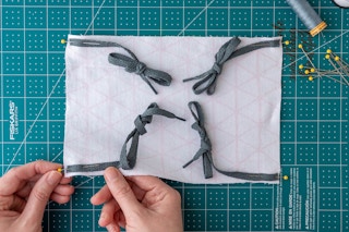 Attaching four pieces of shoelaces, which are tied in bows, to the corners of the fabric with pins.