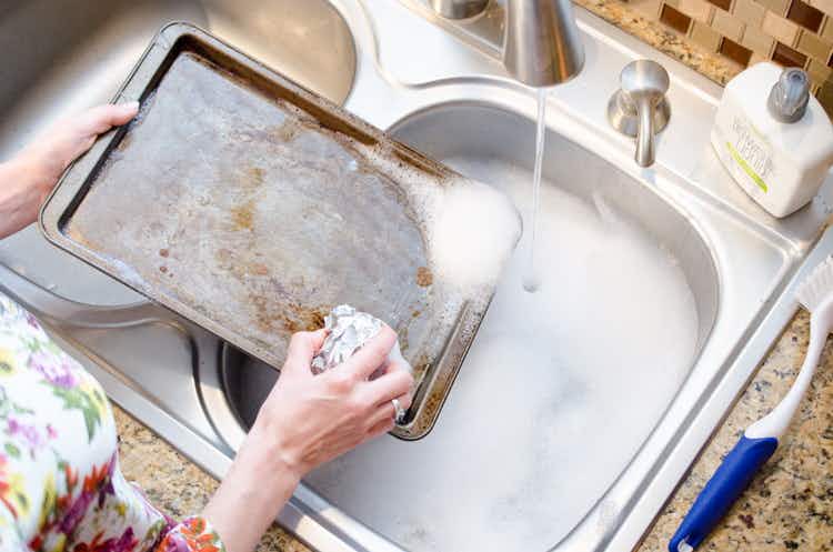 woman-scrubbing-sheet-pan-with-a-crumpled-piece-of-foil-over-a-sink-of-water