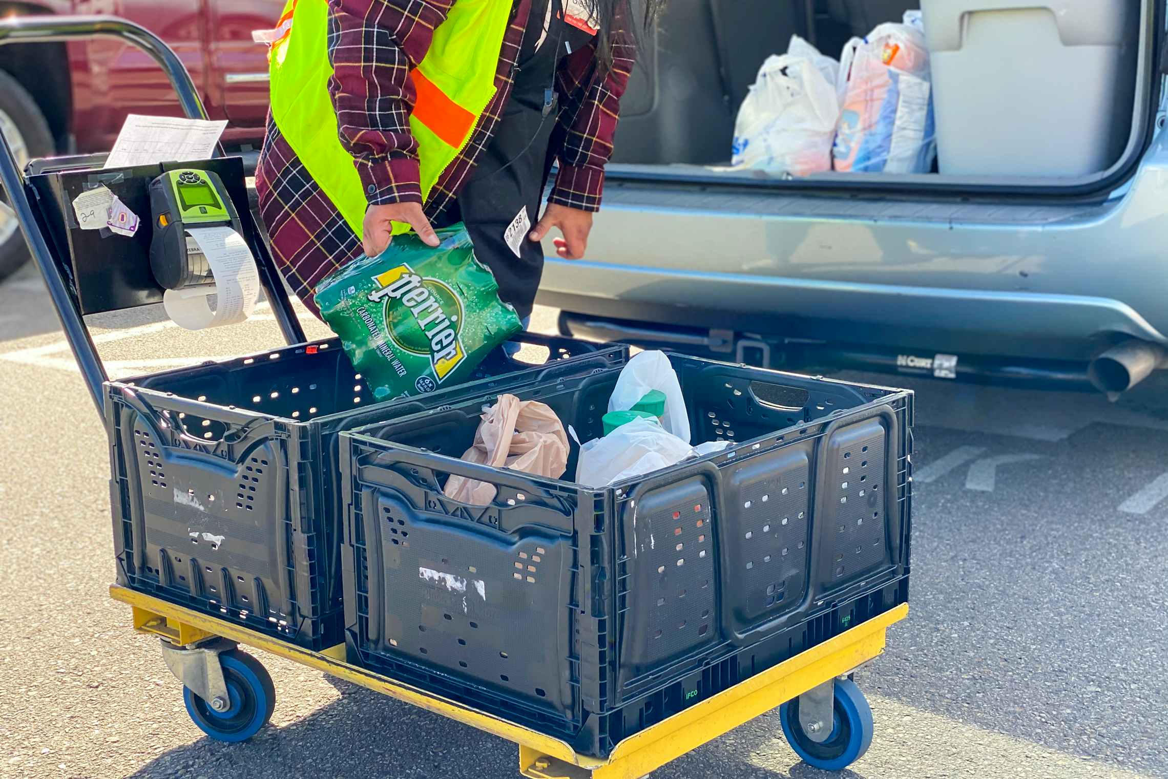 Kroger grocery employee picking up groceries to place in customers open trunk.