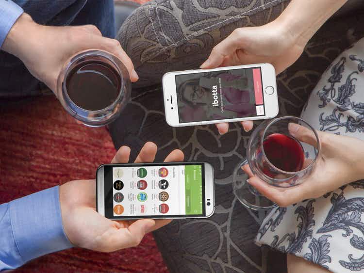 hands hold phones showing ibotta app on screens and hold drinks