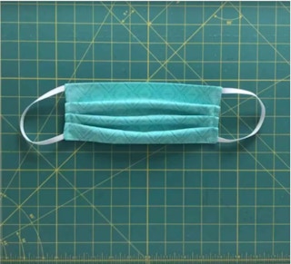 a green home sewn facemask sits on top of a fabric cutting board