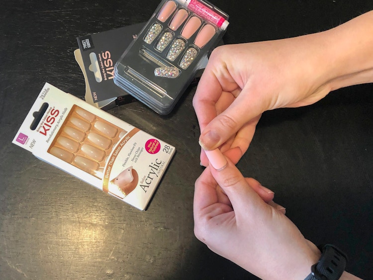A woman applying kiss press on nails to her hands
