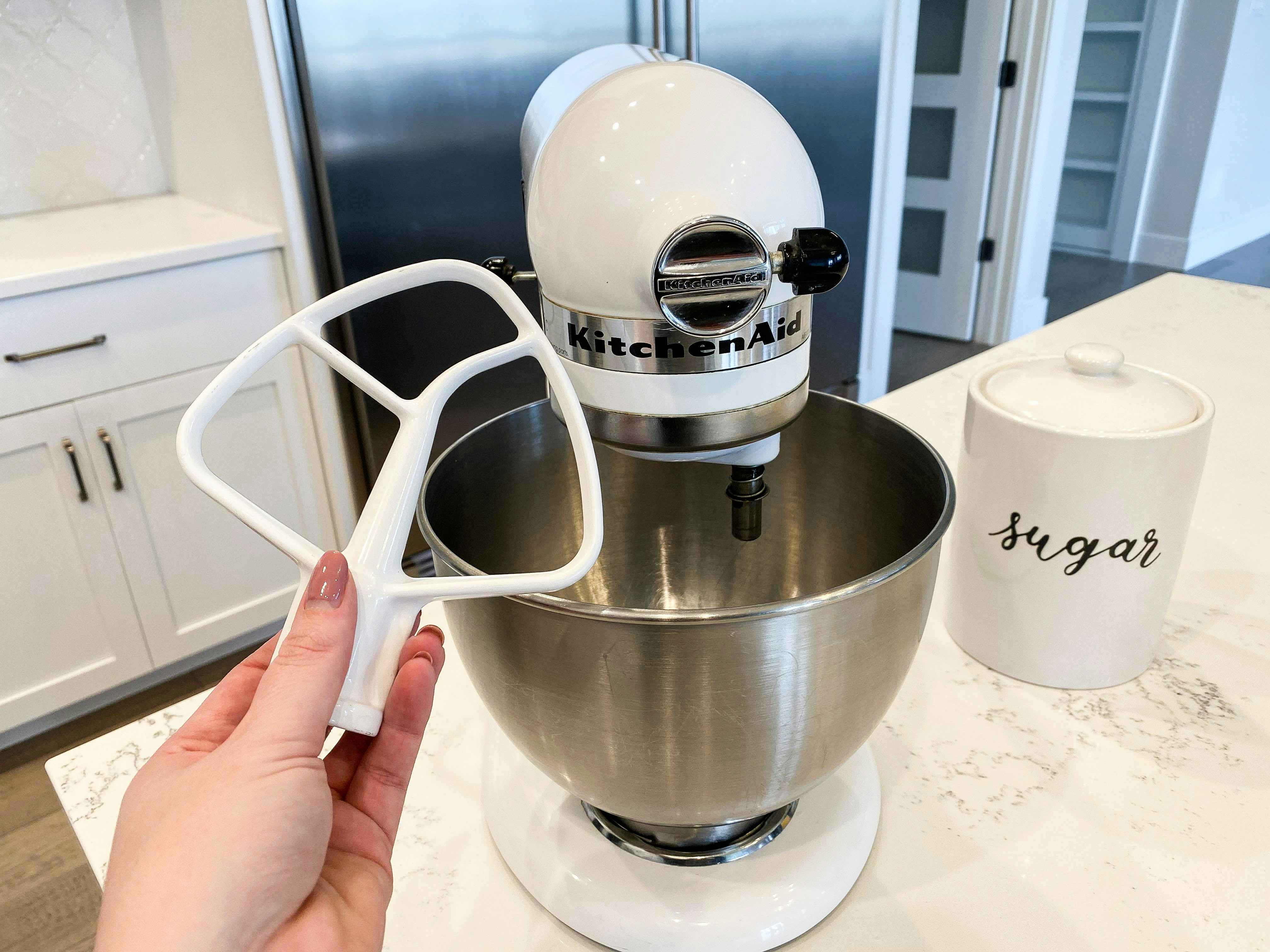 A Kitchenaid mixer on a counter with a hand holding an attachment piece.