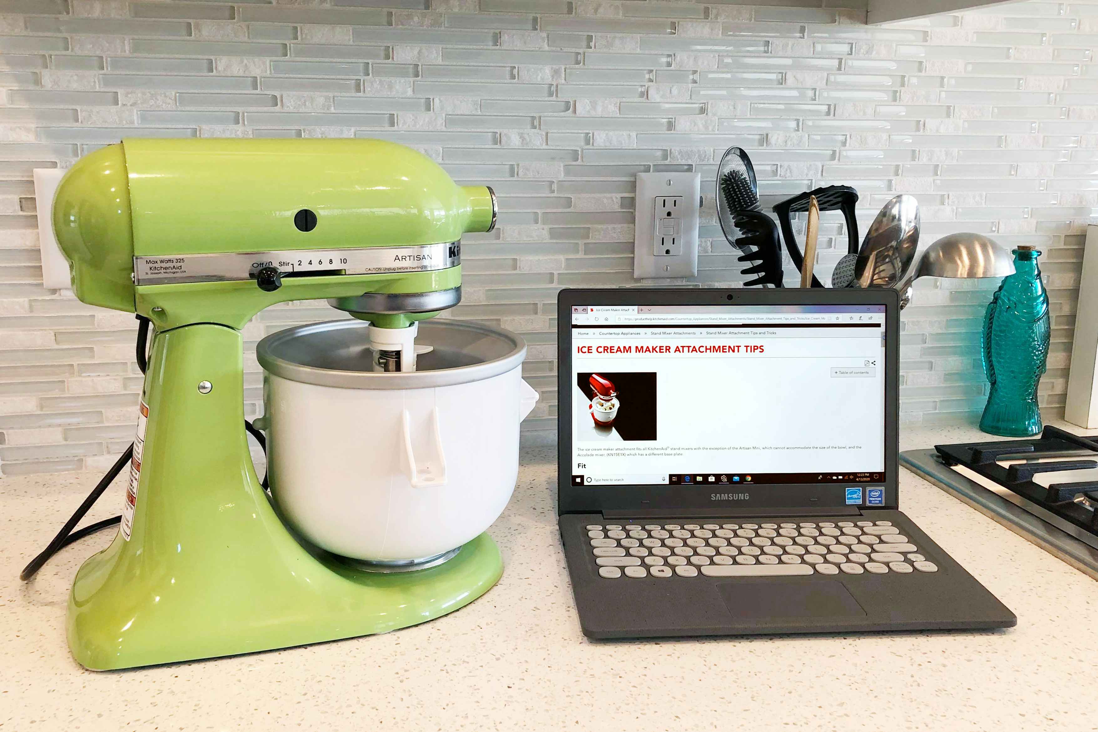 A kitchenaid ice cream maker next to a laptop with an instruction manual on the screen.