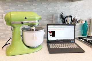 A kitchenaid ice cream maker next to a laptop with an instruction manual on the screen.