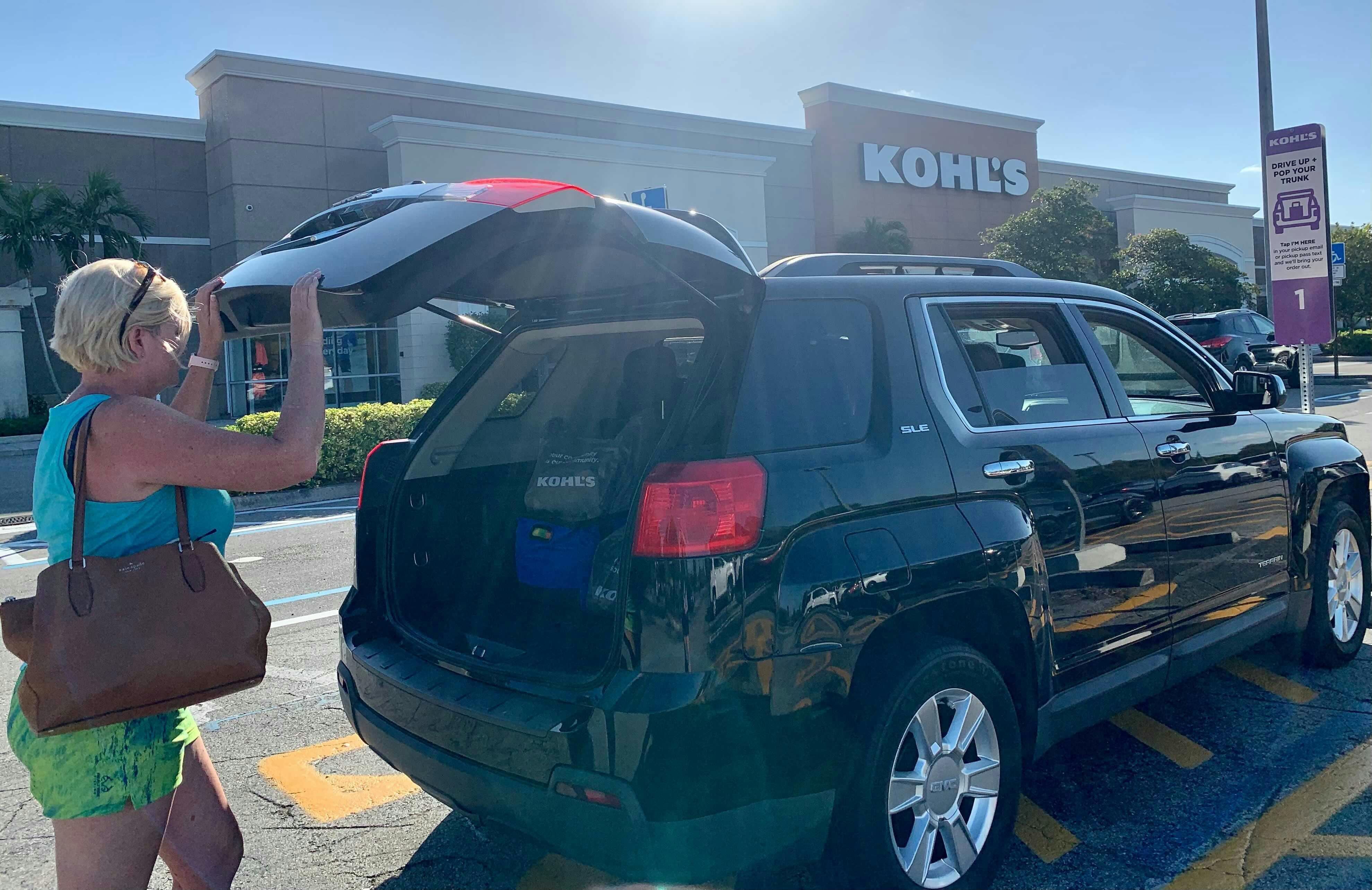 Woman closing trunk of a black midsize suv car parked in pickup parking spots outside of a kohls store
